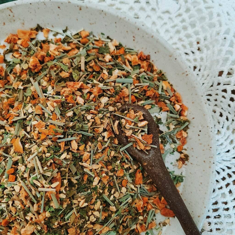 close up view of herbal loose leaf tea in a white bowl and a wooden spoon
