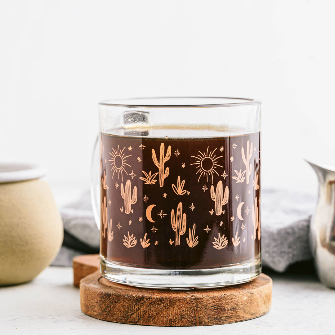 clear glass mug featuring an orange cacti and design on a wooden coaster with a white background