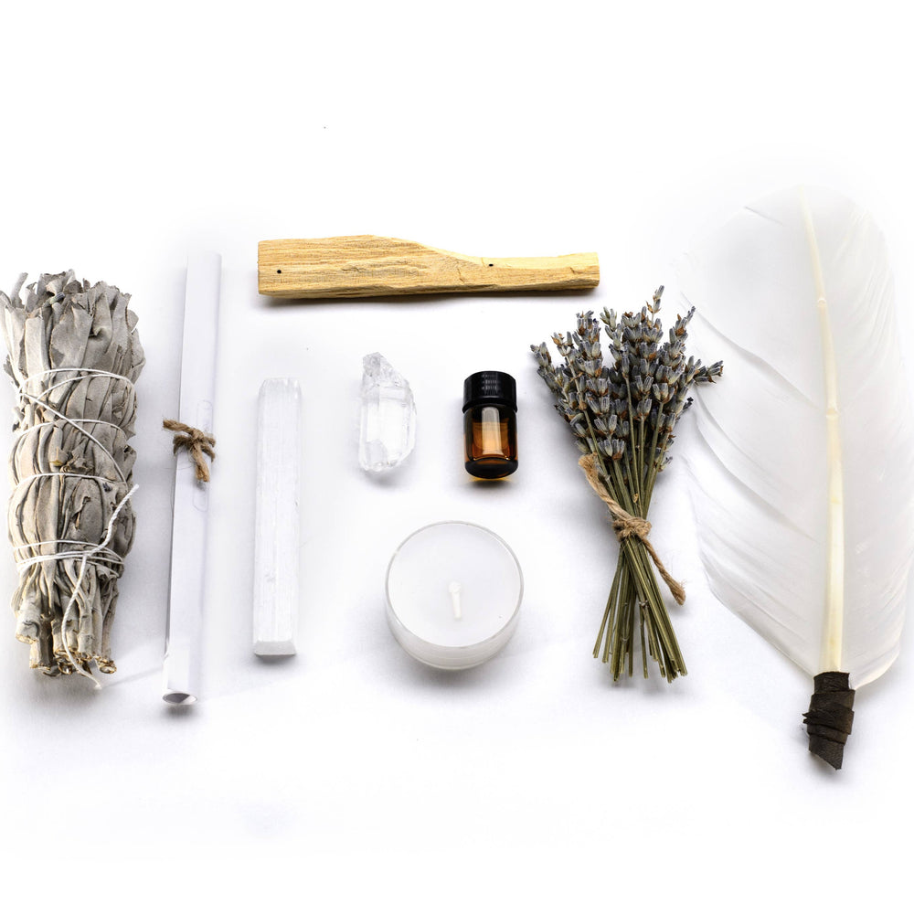 an image of the following items laid out side by side from one another: turkey feather, one yellow candle, two crystals, a bottle of lemon oil, dried herbs and flowers.