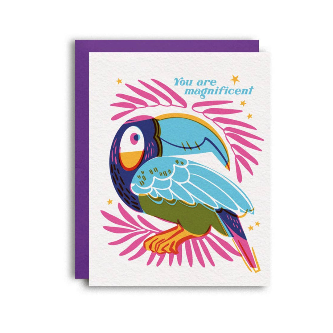 white card with a purple envelope featuring a blue and purple toucan surrounded by pink foilage and the phrase You Are Magnificent in aqua lettering