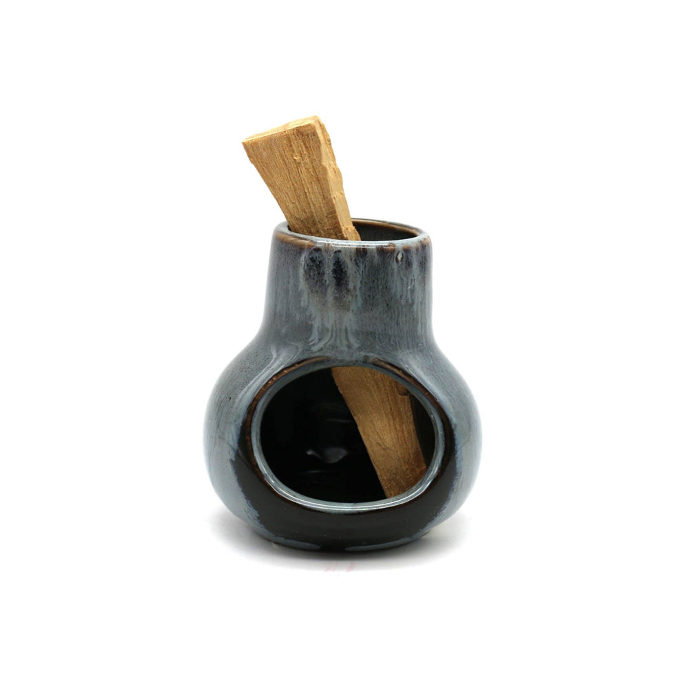 front view of a black ceramic mini chimney with a palo santo stick in it.