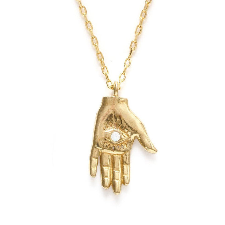 close up view of a gold hand with an eye in the center pendant necklace featuring a crystal in the center of the eye. Brand: Amano Studio