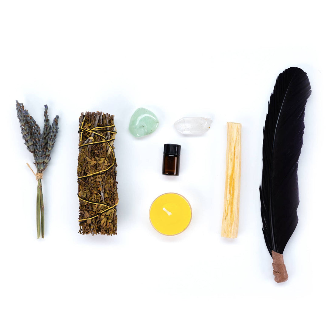 an image of the following items laid out side by side from one another: turkey feather, one yellow candle, two crystals, a bottle of lemon oil, dried herbs and flowers.