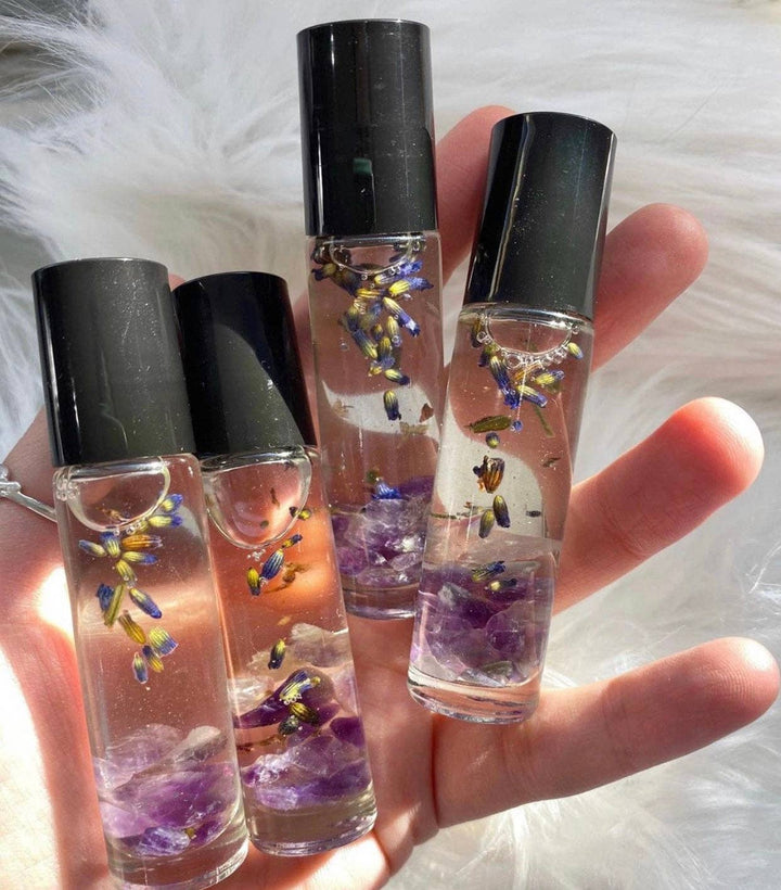 a hand holding 4 clear glass tube of perfume oil with amethyst stones