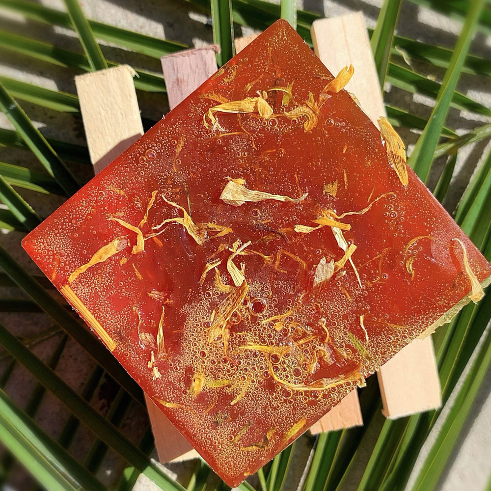 close up view of a dark orange bar of soap with dried flowers embedded in it. Brand: UnTamed Naturals