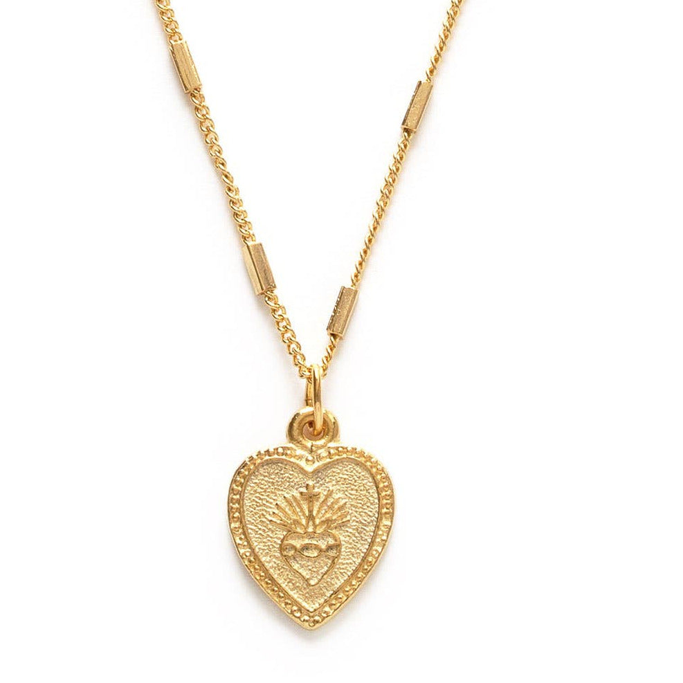 Close up of a gold heart shaped pendant necklace featuring a sacred heart. Brand: Amano Studio
