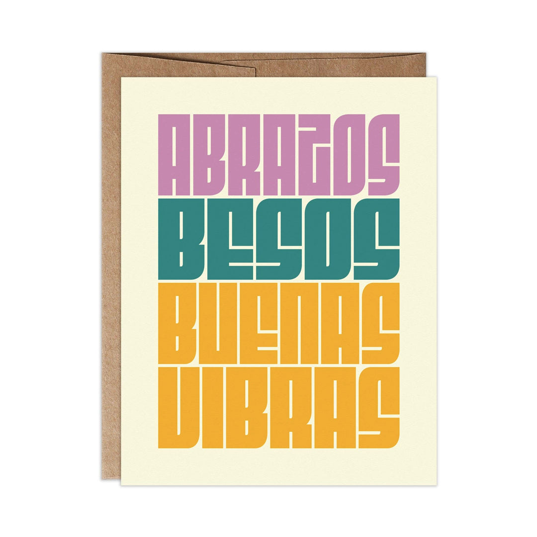 Cream card with a brown envelope and the prase Abrazos, Besos, Buenas Vibras in lavender, teal and gold yellow lettering